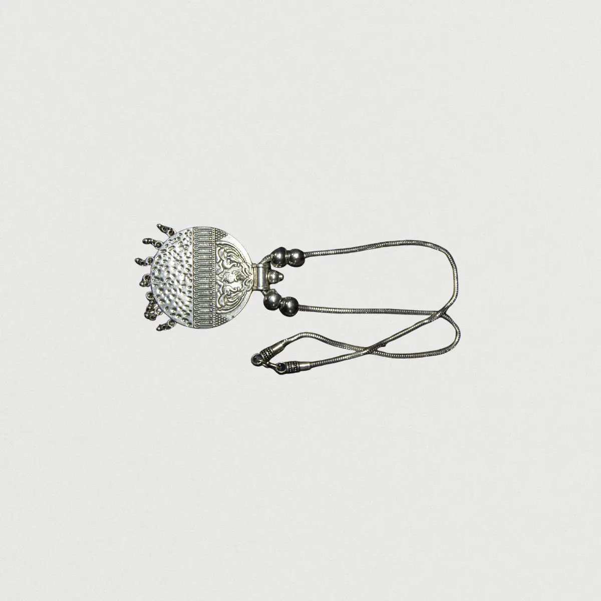 Ornate pineapple pendant necklace with textured design and decorative leaves on chain against neutral background