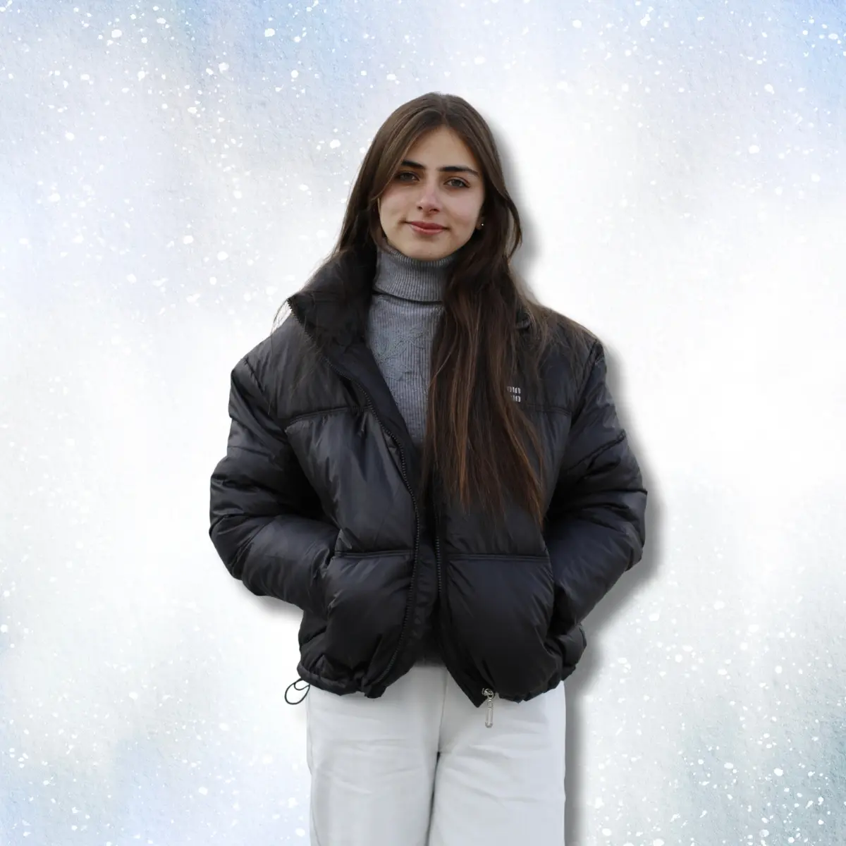 Close-up front view of woman in black cropped puffer jacket with gray turtleneck and white trousers