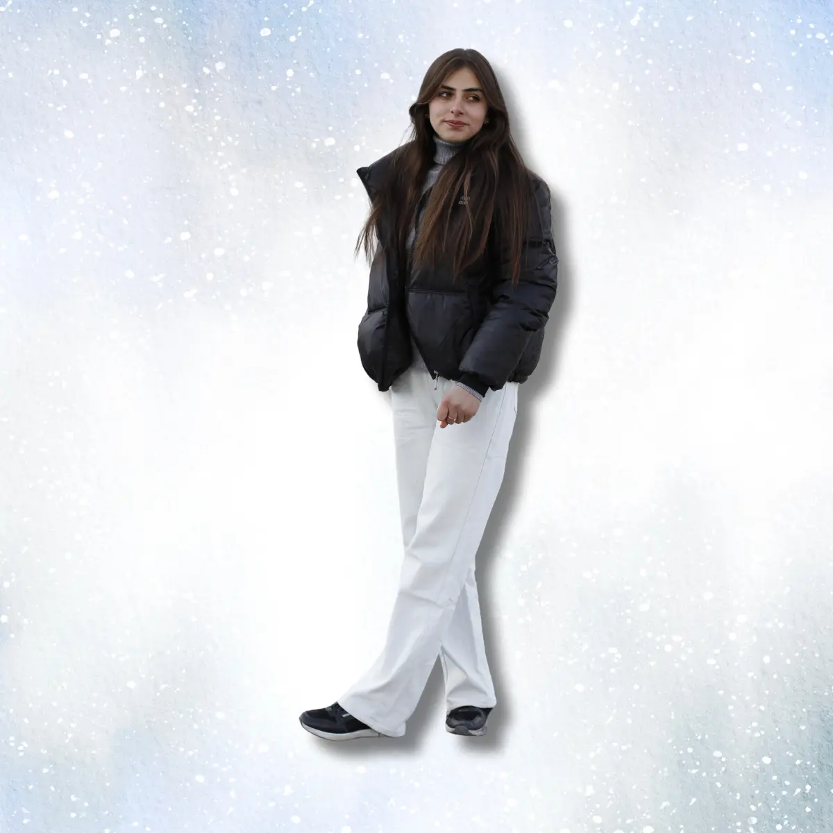 Woman wearing black puffer jacket, gray turtleneck sweater, and white wide leg pants on rocky terrain